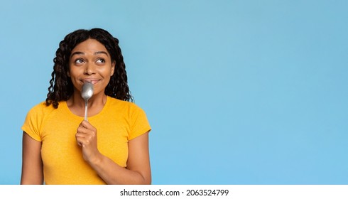 Excited And Hungry Young African American Woman With Spoon In Her Mouth Looking At Copy Space, Dreaming About Delicious Healthy Food, Choosing Something To Eat, Blue Studio Background, Panorama