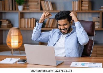 Excited indian business man looking at laptop celebrating win accomplishment victory with yes gesture. Happy arab executive feeling winner checking crypto market investment growth in office - Powered by Shutterstock