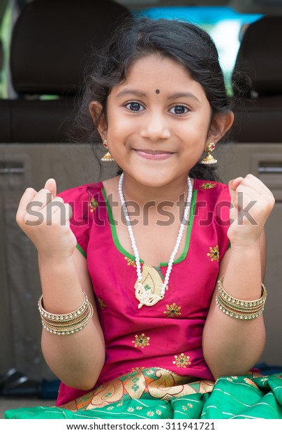 Excited Indian girl sitting in car\
smiling, ready to vacation. Asian child in traditional\
dress.