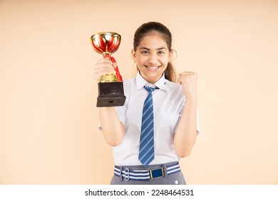 Excited Indian student schoolgirl wearing school uniform holding victory trophy in hand isolated on beige background, Studio shot, closeup, Education concept. - Powered by Shutterstock