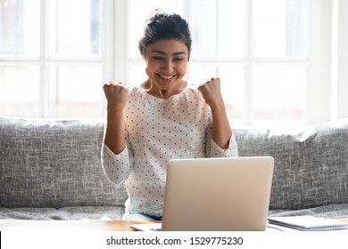 Excited Indian Woman Celebrating Win, Looking At Laptop Screen, Sitting On Couch At Home, Happy Girl Reading Good News In Email, Great Sale Shopping Offer, Student Receiving Positive Exam Results