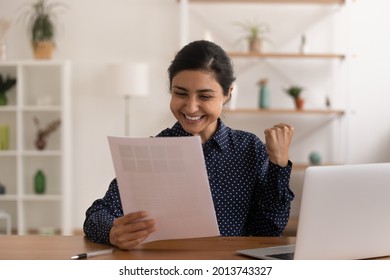 Excited Indian Woman Reading Good News In Letter, Rejoicing Success, Sitting At Work Desk With Laptop, Overjoyed Smiling Young Female Student Or Businesswoman Received Job Promotion Or Scholarship