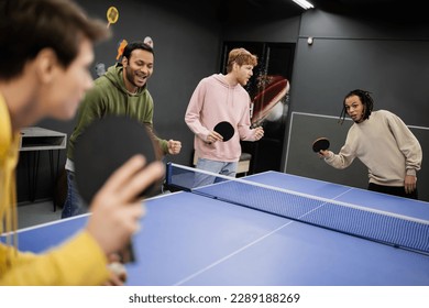 Excited interracial men standing near friends playing table tennis in gaming club - Powered by Shutterstock