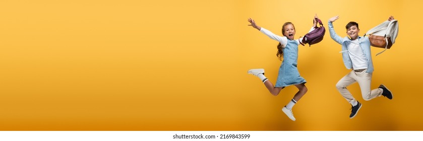 Excited interracial schoolkids with backpacks jumping on yellow background, banner - Shutterstock ID 2169843599