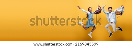 Excited interracial schoolkids with backpacks jumping on yellow background, banner