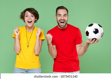 Excited joyful couple friends sport family woman man football fans in yellow red t-shirts cheer up support favorite team with soccer ball doing winner gesture isolated on green background studio - Shutterstock ID 1873451140