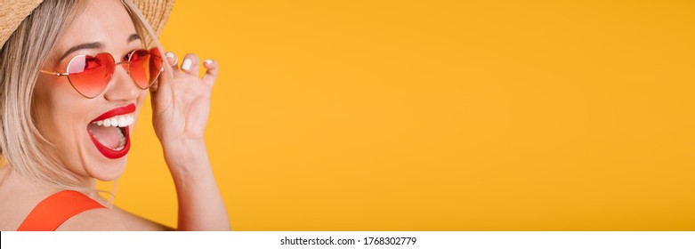 Excited Joyful Happy Emotional Blonde Woman Close Up Portrait On Yellow Background. Fashionable Bright Heart Shaped Pink Sunglasses. Open Mouth Big Red Lips Teeth Smile. Horizontal Long Banner