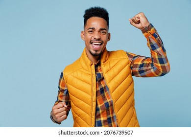 Excited jubilant joyful young black man 20s years old wears yellow waistcoat shirt doing winner gesture celebrate clenching fists say yes isolated on plain pastel light blue background studio portrait