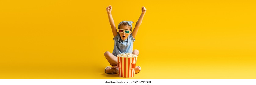 Excited Kid In 3d Glasses Sitting With Crossed Legs And Raised Hands Near Popcorn Bucket And Watching Movie On Yellow, Banner