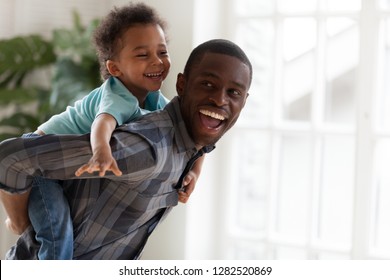 Excited kid boy playing with happy african american father at home, cheerful black dad piggybacking cute child carrying little son on back having fun on weekend spending time together with daddy - Powered by Shutterstock