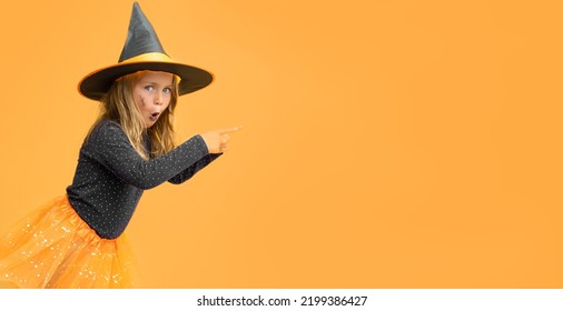 Excited Kid Girl Wearing Witch Black Hat Costume Halloween Isolated Yellow Studio Background With Finger Pointed Up.Seasonal Sale And Discount. Shopping Attentive. Banner, Copy Space For Text, Mock Up