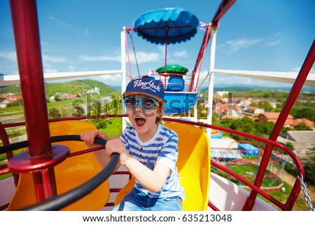 excited kid riding on ferris wheel in amusement park