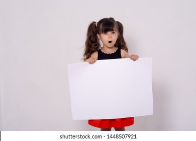 Excited Kid With White Template. Advertising Place For You, Empty Card, Cute Kid Holding It. Photo Of Positive Schoolkid Behind Partition Looking At Camera.