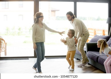 Excited kids playing hide and seek active game with blindfolded mom, happy family having fun together in living room of luxury country house, parents and children leisure weekend activities concept