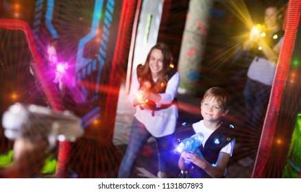 Excited Kids And Theirs Parents In Bright Beams Of Laser Guns During Laser Tag Game In Dark Room
