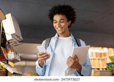 Excited Latin student guy holding textbook and reading text message on cellphone, standing in university library and smiling - Powered by Shutterstock