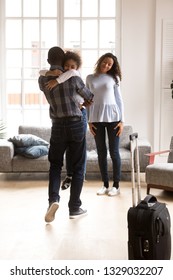 Excited Little African American Daughter Hug Young Father Meeting Him Come Home From Business Trip, Happy Black Mother And Kid Smiling Glad To Reunite With Dad, Embracing Him. Family Reunion Concept