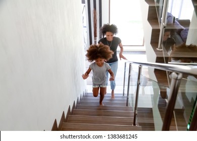 Excited Little African American Girl Run Up Stairs Of New Home With Young Mom, Happy Black Mother And Small Daughter Explore Bought House On Moving Day Together, Mommy Have Fun Playing With Kid