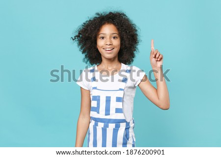 Excited little african american kid girl 12-13 years old in striped clothes isolated on blue background. Childhood lifestyle concept. Mock up copy space. Holding index finger up with great new idea