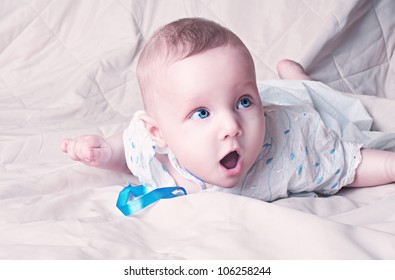 Excited Little Baby Boy With Wide Open Blue Eyes Laying On Blanket