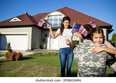 Excited little caucasian girl running to her military father in front of the house while woman waving with American flags. - Powered by Shutterstock