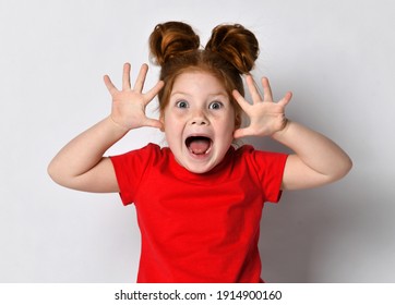 Excited Little girl with freckles and red hair screams loudly with raised arms, looking at the camera. Portrait of emotional child on gray background. The concept of childrens hysterics and emotions.