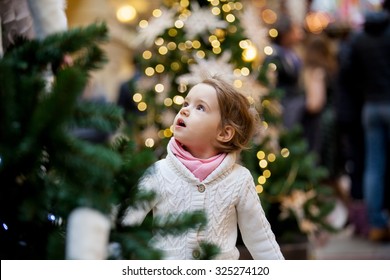 Excited Little Girl With Open Mouth Looking At The Beautifully Decorated Christmas Trees With Lights In The Shopping Mall