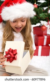 Excited Little Girl Opening Christmas Present In Front Of The Fir Tree - Closeup