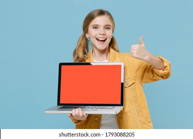 Excited little kid girl 12-13 years old in yellow jacket isolated on blue background. Childhood lifestyle concept. Mock up copy space. Hold laptop pc computer with blank empty screen showing thumb up