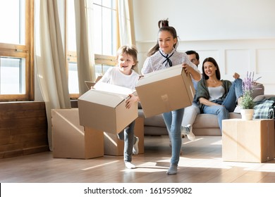 Excited Little Kids Run Carry Cardboard Boxes Feel Overjoyed On Moving Day To Own Dwelling, Happy Small Children Have Fun Unpack Packages In Living Room Settle Relocating To New House With Parents