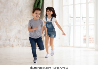 Excited Little Preschooler Brother And Sister Have Fun In Empty Living Room Moving To New House, Happy Small Boy And Girl Play Running Around Own Home Overjoyed To Relocate. Relocation Concept