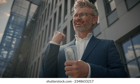 Excited lucky winner wealthy happy rich old middle-aged businessman hold money cash celebrate financial achievement outdoor mature senior man business financial success achieve winning gesture in city - Shutterstock ID 2348653217