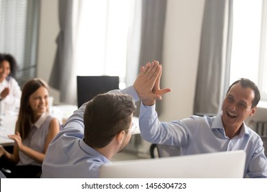 Excited male colleagues give high five celebrating shared business success working online, happy coworkers or businessmen join hands congratulating with goal achievement or shared win or triumph