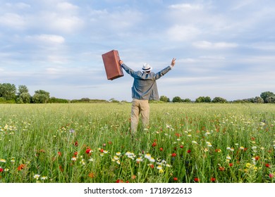 Excited Male On Farmland Sunset Natural Outdoors Background. Unrecognized Hopeful Person Holding Suitcase Backview, Traveling Away Coming Back Scene. White Clouds Blooming Flowers Relaxing Freedom. 