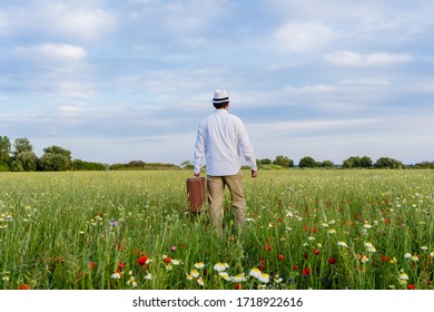 Excited Male On Farmland Sunset Natural Outdoors Background. Unrecognized Hopeful Person Holding Suitcase Backview, Traveling Away Coming Back Scene. White Clouds Blooming Flowers Relaxing Freedom. 