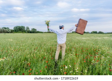 Excited Male On Farmland Sunset Natural Outdoors Background. Unrecognized Hopeful Person Holding Suitcase Backview, Traveling Away Coming Back Scene. White Clouds Blooming Flowers Relaxing Freedom. 