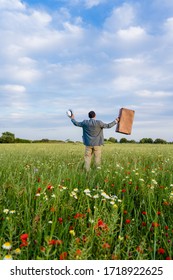 Excited Male On Farmland Sunset Natural Outdoors Background. Unrecognized Hopeful Person Holding Suitcase Backview, Traveling Away Coming Back Scene. White Clouds Blooming Flowers Relaxing Freedom. 