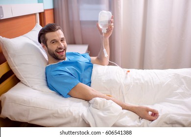 Excited Male Patient Lying In Hospital Bed And Holding Drop Counter 