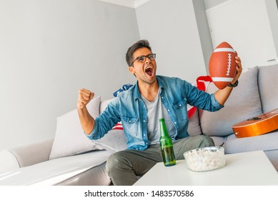 Excited Man Cheering While Watching American Football Match On Sofa. Man  Watching Rugby Match Victory. Gay Watching American Football Match On Television At Home. 