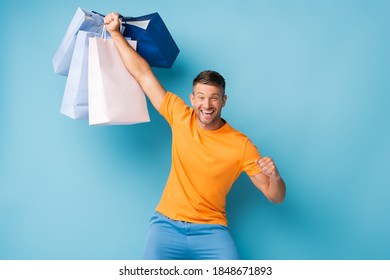 Excited Man In T-shirt Holding Shopping Bags On Blue