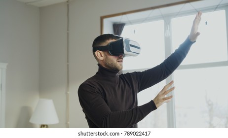 Excited man with virtual reality headset playing 360 video game at home