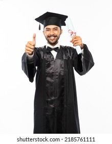 Excited man wearing toga with thumbs up holding diploma paper on white background