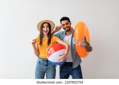 Excited married couple standing with an inflatable circle and ball on light background wall, free space. People and summer vacation concept