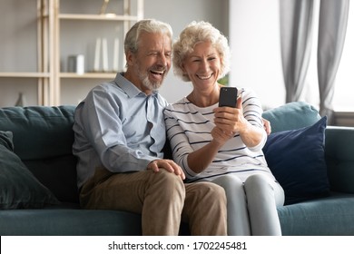 Excited Mature Couple Having Fun With Phone Together, Posing For Photo, Taking Selfie, Smiling Older Woman Holding Smartphone, Looking At Screen, Watching Funny Video, Sitting On Cozy Couch