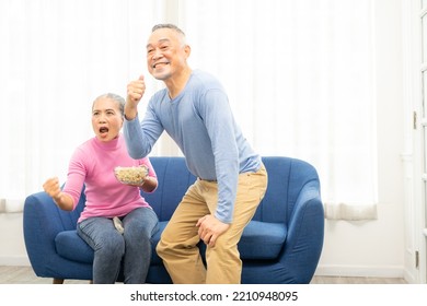 Excited Mature Couple, Senior Man And Woman Watching Tv, Senior Sport Fans Celebrating Favorite Team Victory, Sitting On Cozy Couch And Eating Popcorn Snack At Home, Enjoying Weekend. Happy Senior.