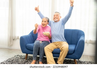 Excited Mature Couple, Senior Man And Woman Watching Tv, Senior Sport Fans Celebrating Favorite Team Victory, Sitting On Cozy Couch And Eating Popcorn Snack At Home, Enjoying Weekend. Happy Senior.