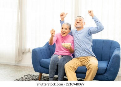 Excited Mature Couple, Senior Man And Woman Watching Tv, Senior Sport Fans Celebrating Favorite Team Victory, Sitting On Cozy Couch And Eating Popcorn Snack At Home, Enjoying Weekend. Happy Senior.