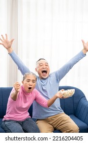 Excited Mature Couple, Senior Man And Woman Watching Tv, Senior Sport Fans Celebrating Favorite Team Victory, Sitting On Cozy Couch And Eating Popcorn Snack At Home, Enjoying Weekend. Happy Senior.