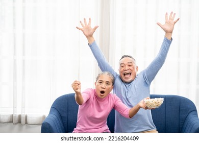 Excited Mature Couple, Senior Man And Woman Watching Tv, Senior Sport Fans Celebrating Favorite Team Victory, Sitting On Cozy Couch And Eating Popcorn Snack At Home, Enjoying Weekend. Happy Senior.