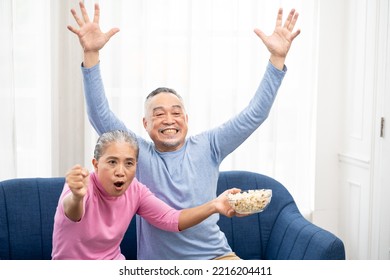 Excited Mature Couple, Senior Man And Woman Watching Tv, Senior Sport Fans Celebrating Favorite Team Victory, Sitting On Cozy Couch And Eating Popcorn Snack At Home, Enjoying Weekend. Happy Senior.